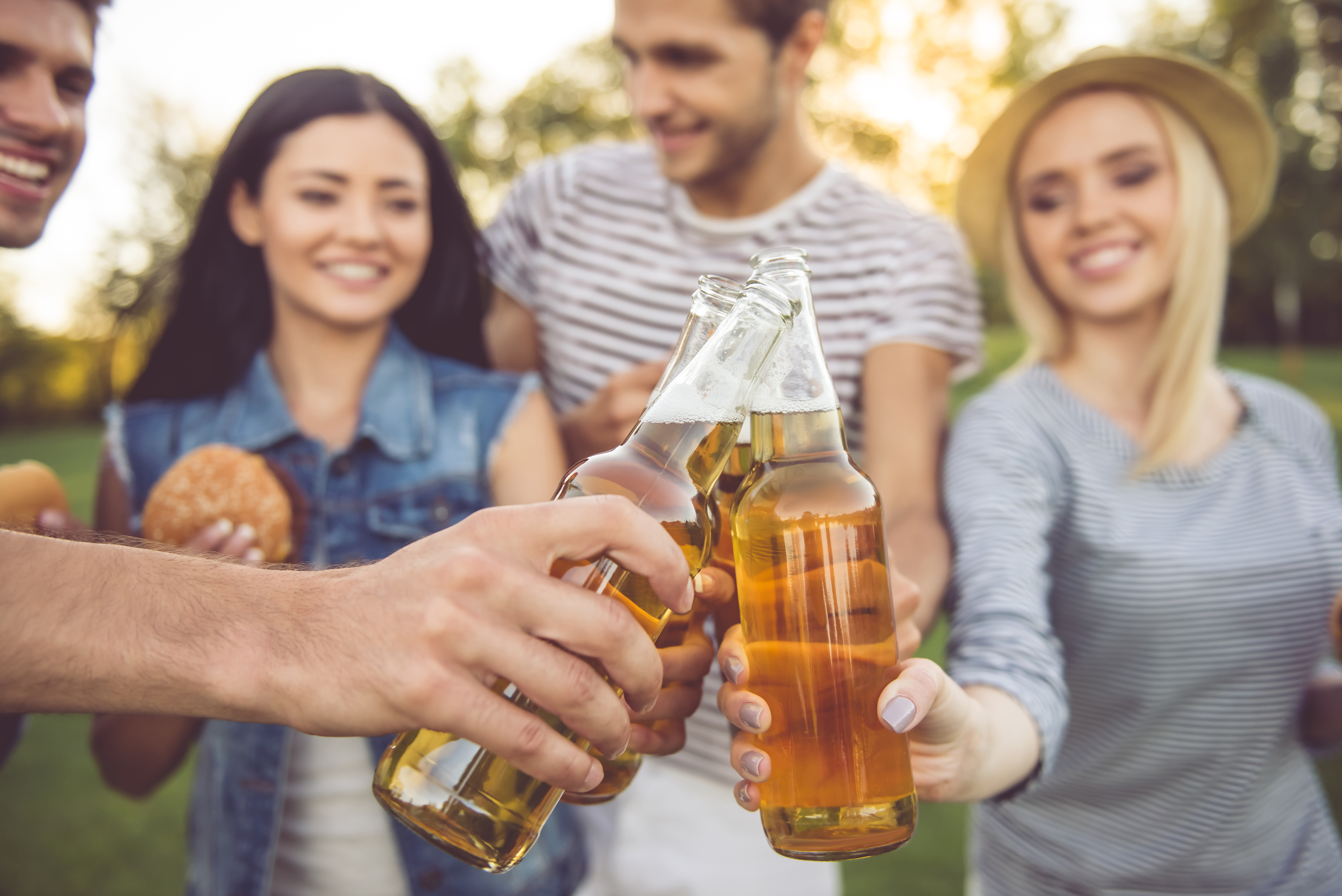 Friends toasting with bottles of beer in a park.
