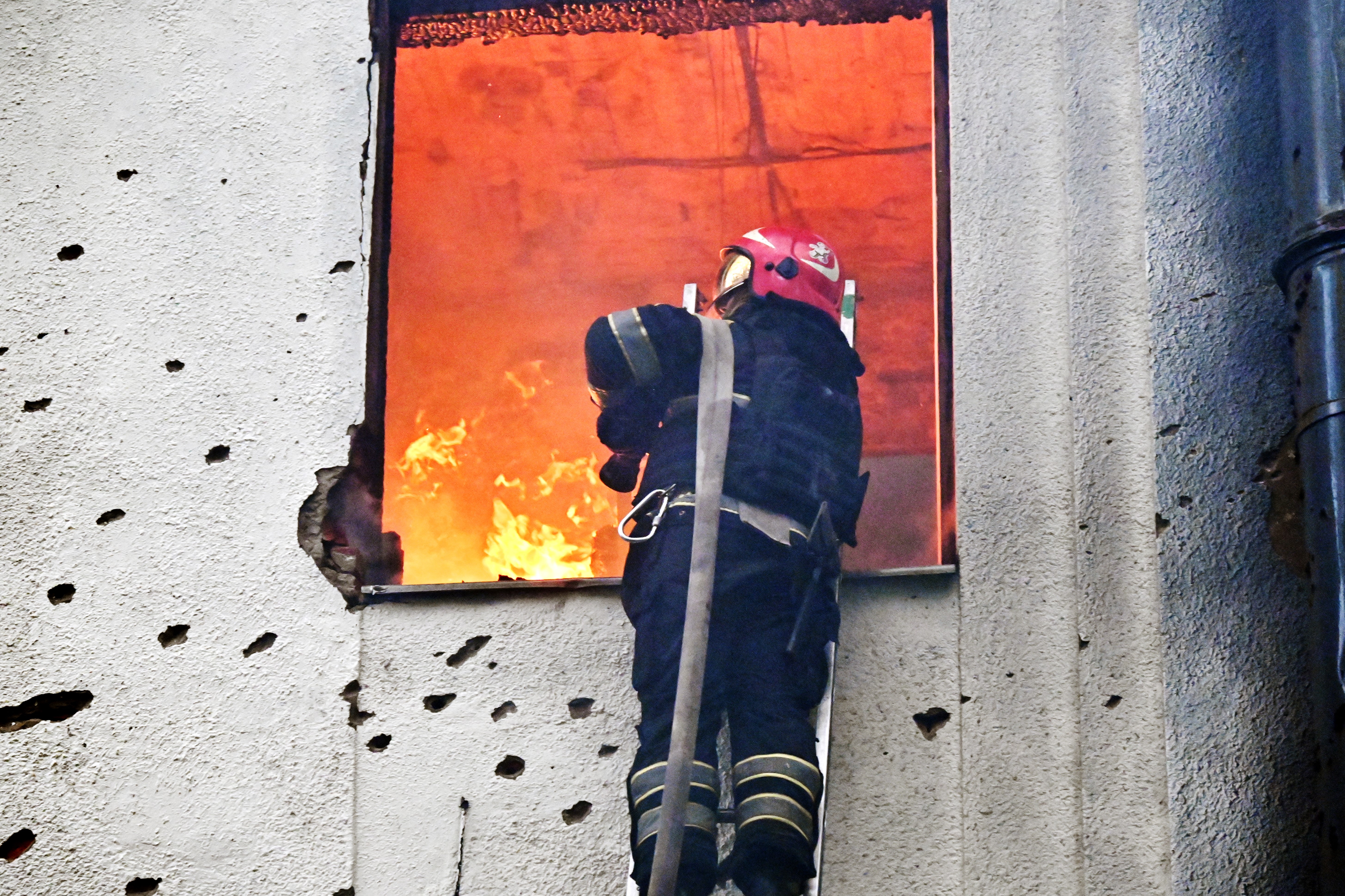 Firefighter battling a fire in a bullet-ridden building.