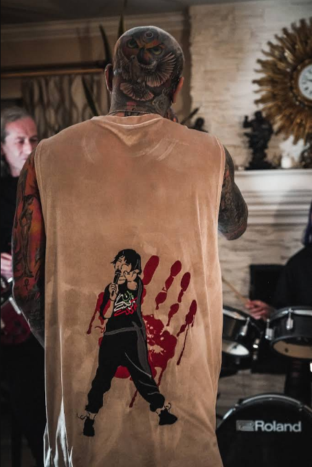 Person with a large back tattoo wearing a sleeveless shirt with a graphic of a person singing on it.