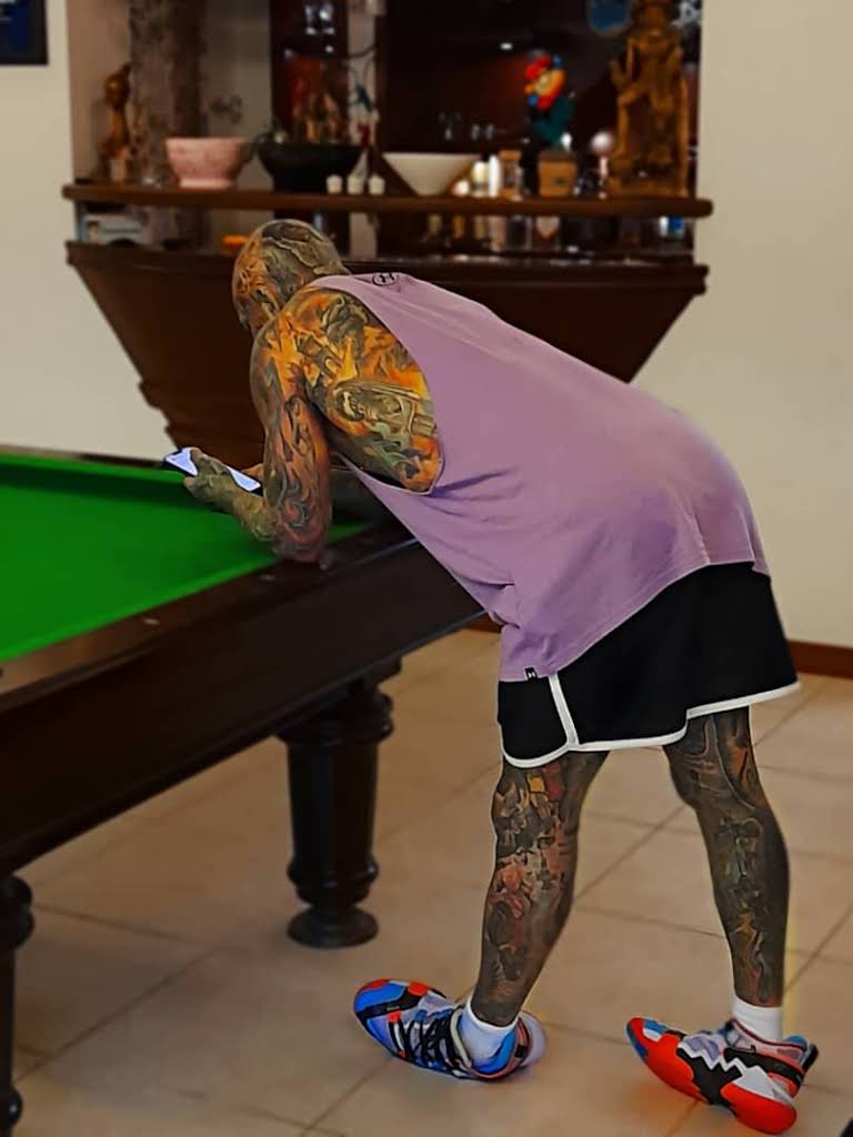 Man with tattoos looking at his phone next to a pool table.