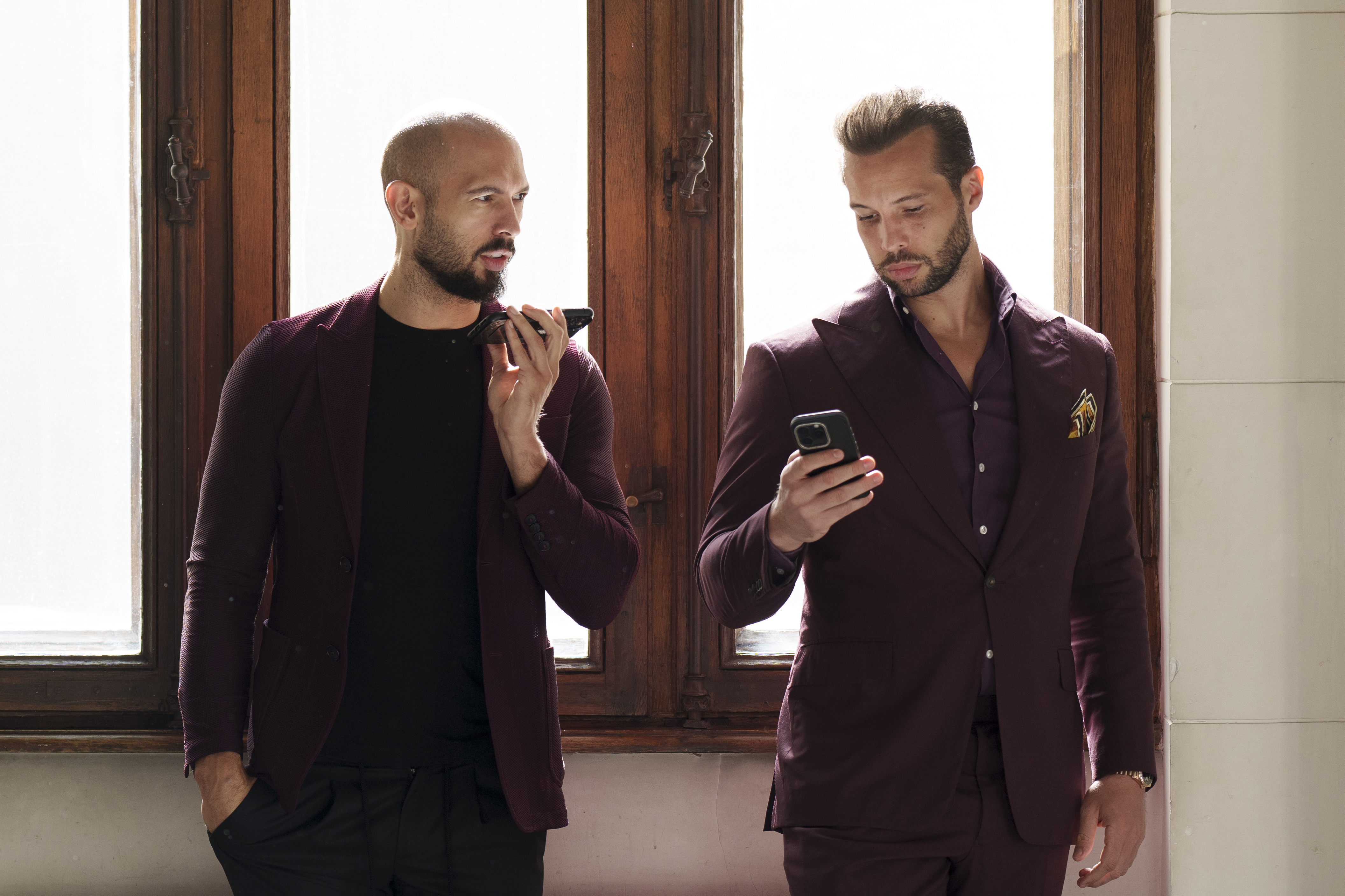 Two men in maroon suits using smartphones.