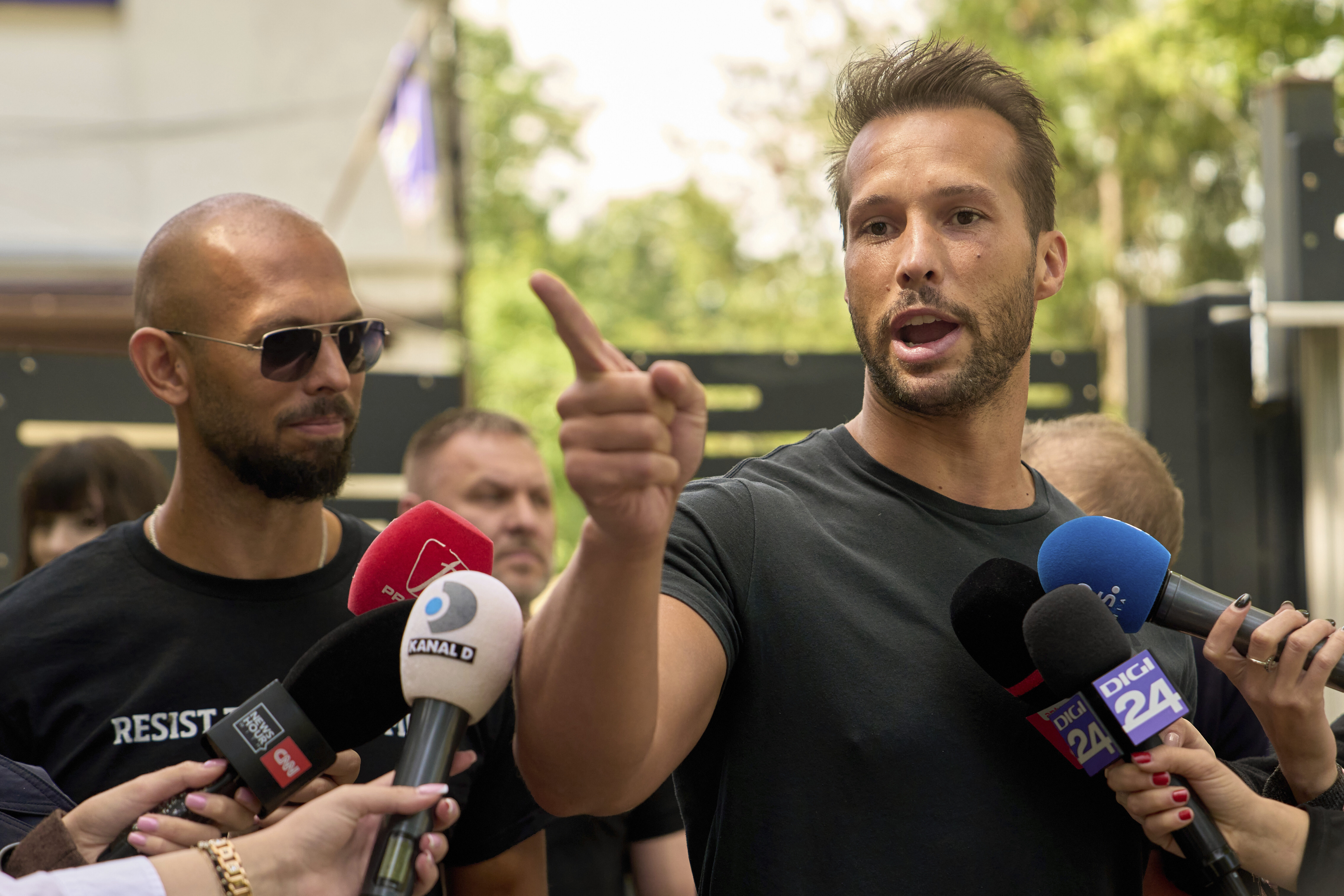 Tristan Tate speaks to reporters as older brother, Andrew, looks on outside a police station on May 21, 2025.