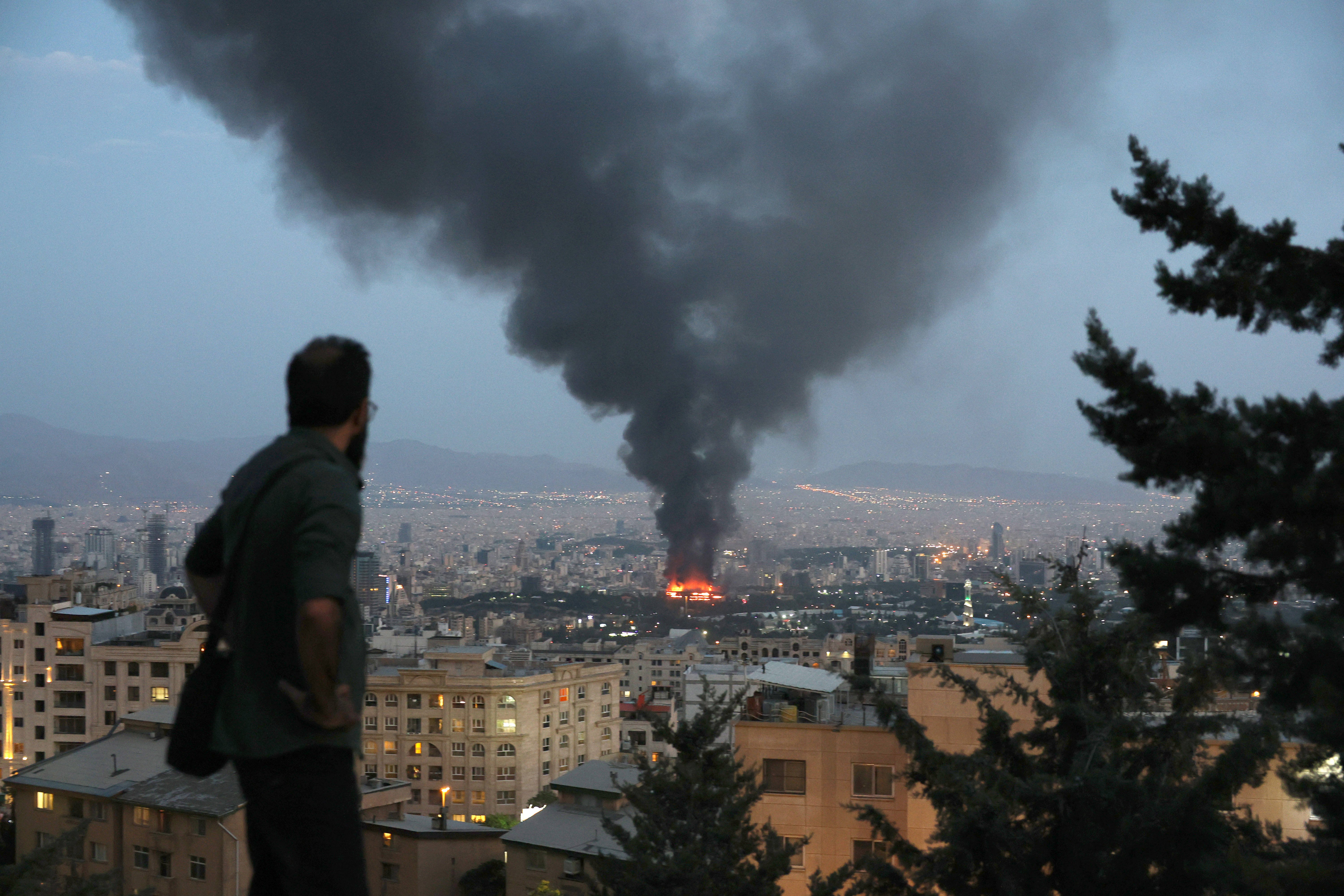A man watches smoke billowing from a burning building in Tehran, Iran.