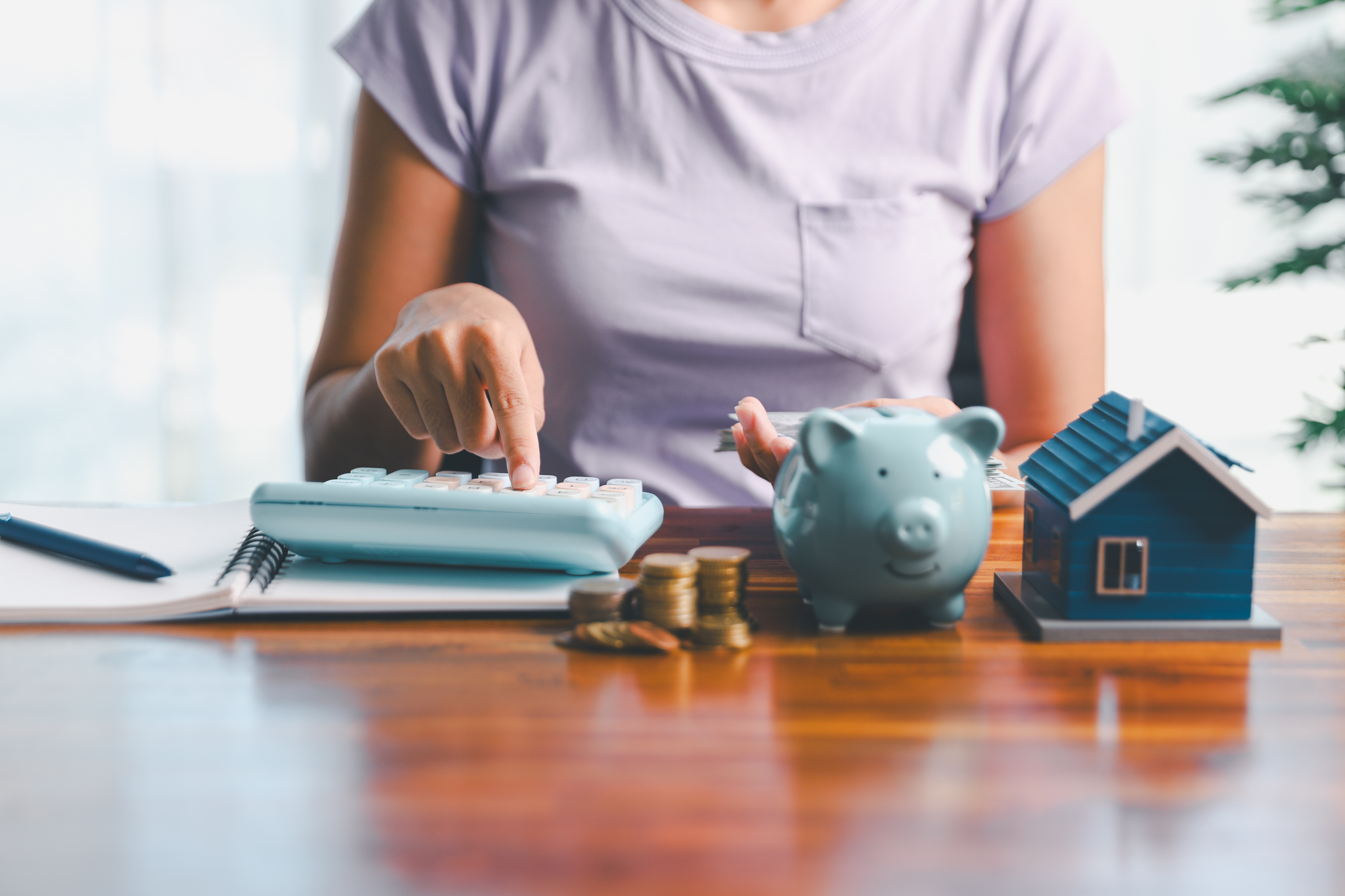 Woman using calculator, saving money in piggy bank for house.