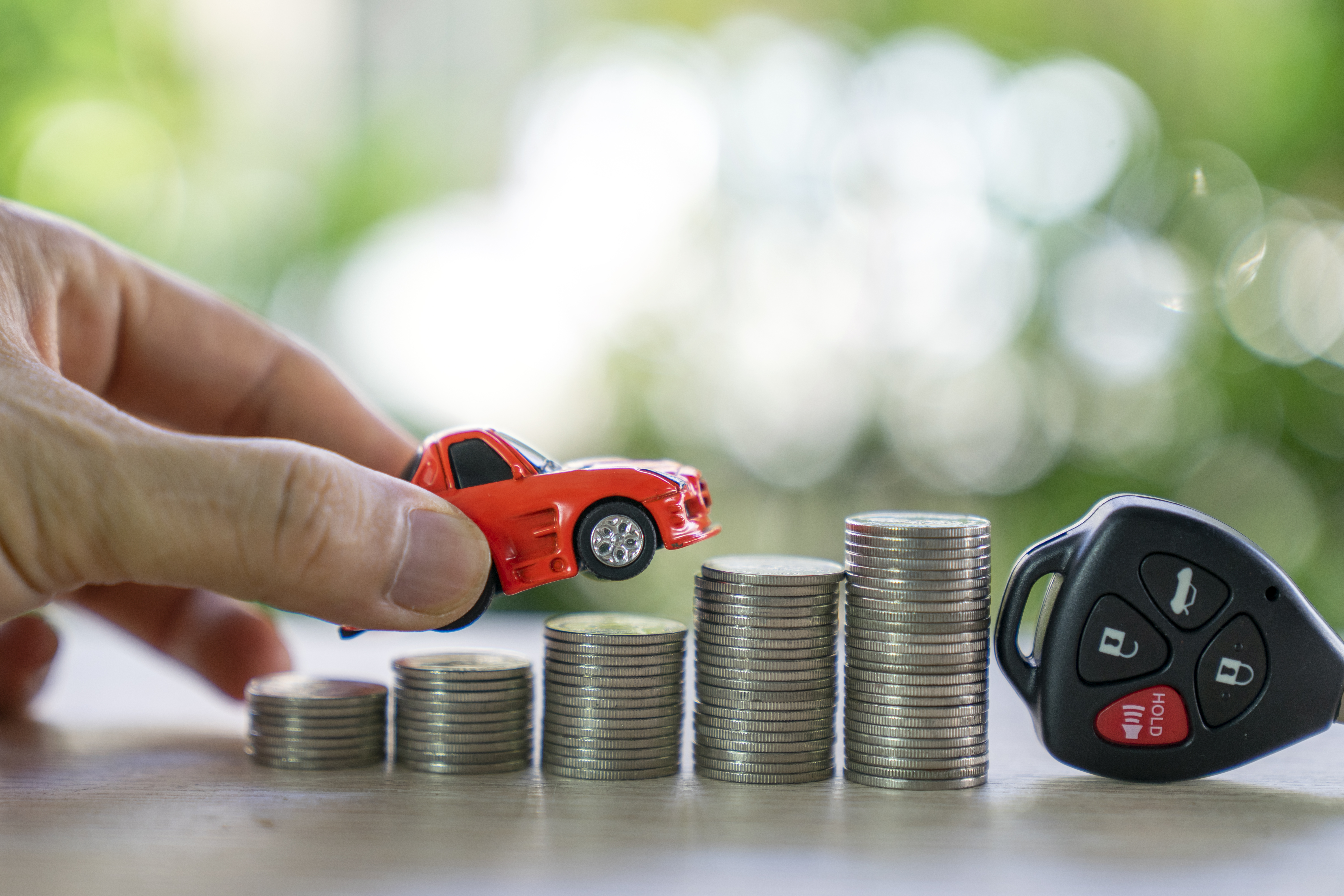 A hand placing a toy car on stacks of coins next to a car key; concept of car loan and insurance.