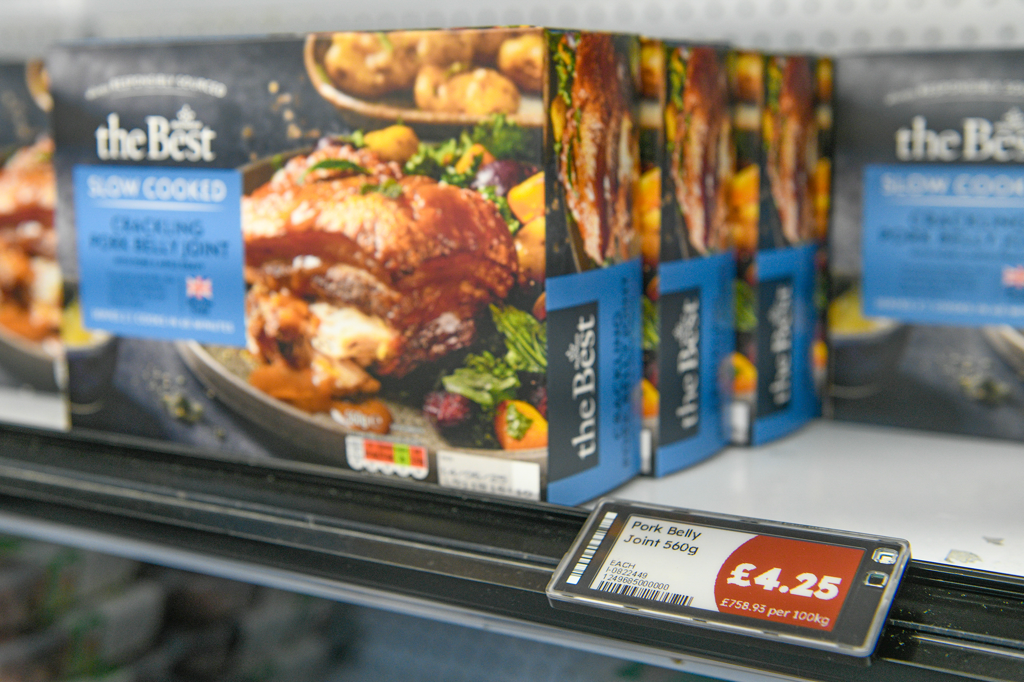 Frozen pork belly joint packages on a supermarket shelf with price tag.
