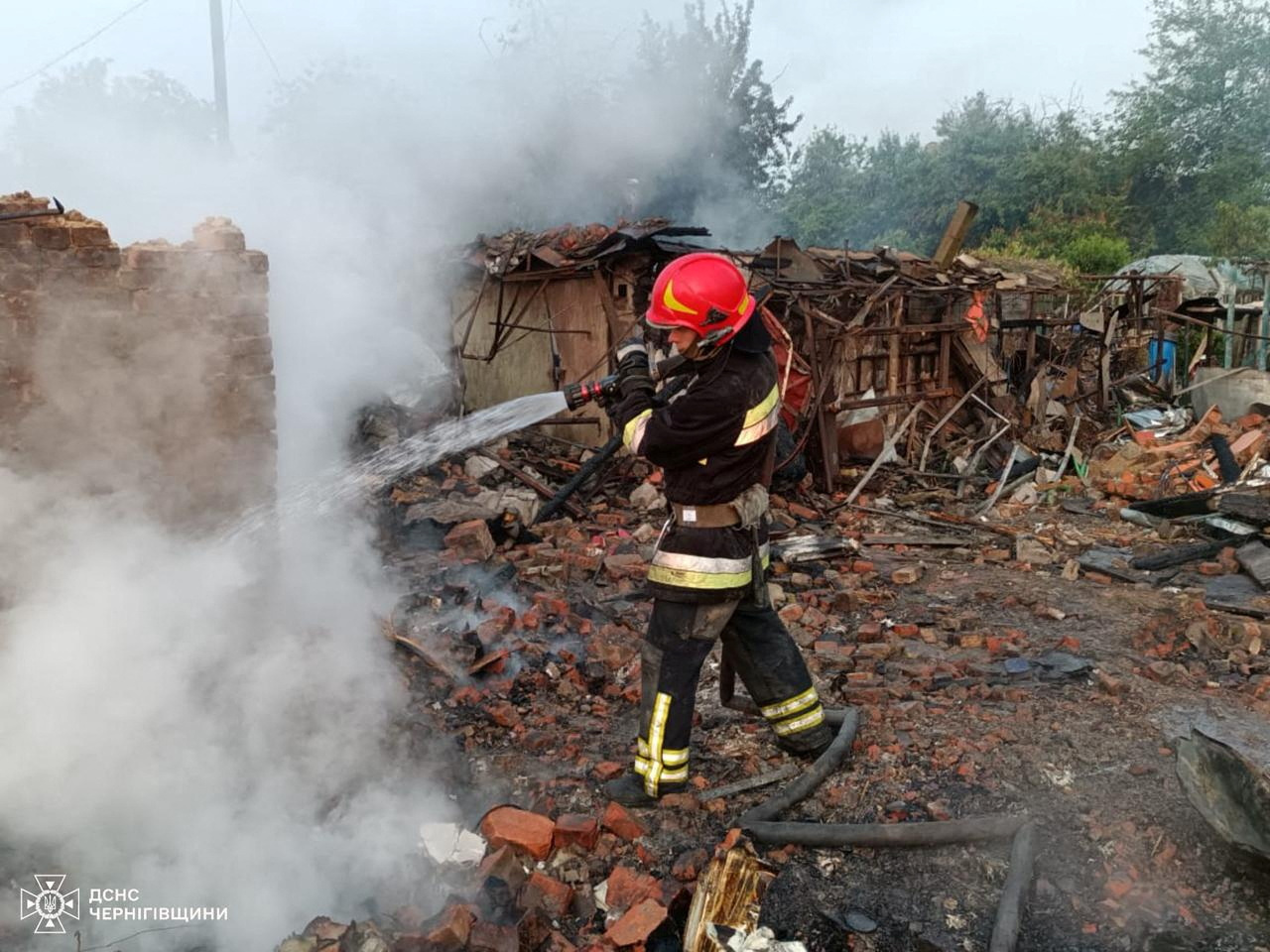 Firefighters extinguish a flame near the remains of a destroyed building.