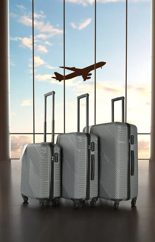 Three gray suitcases in front of an airport window with a plane silhouetted in the sky.
