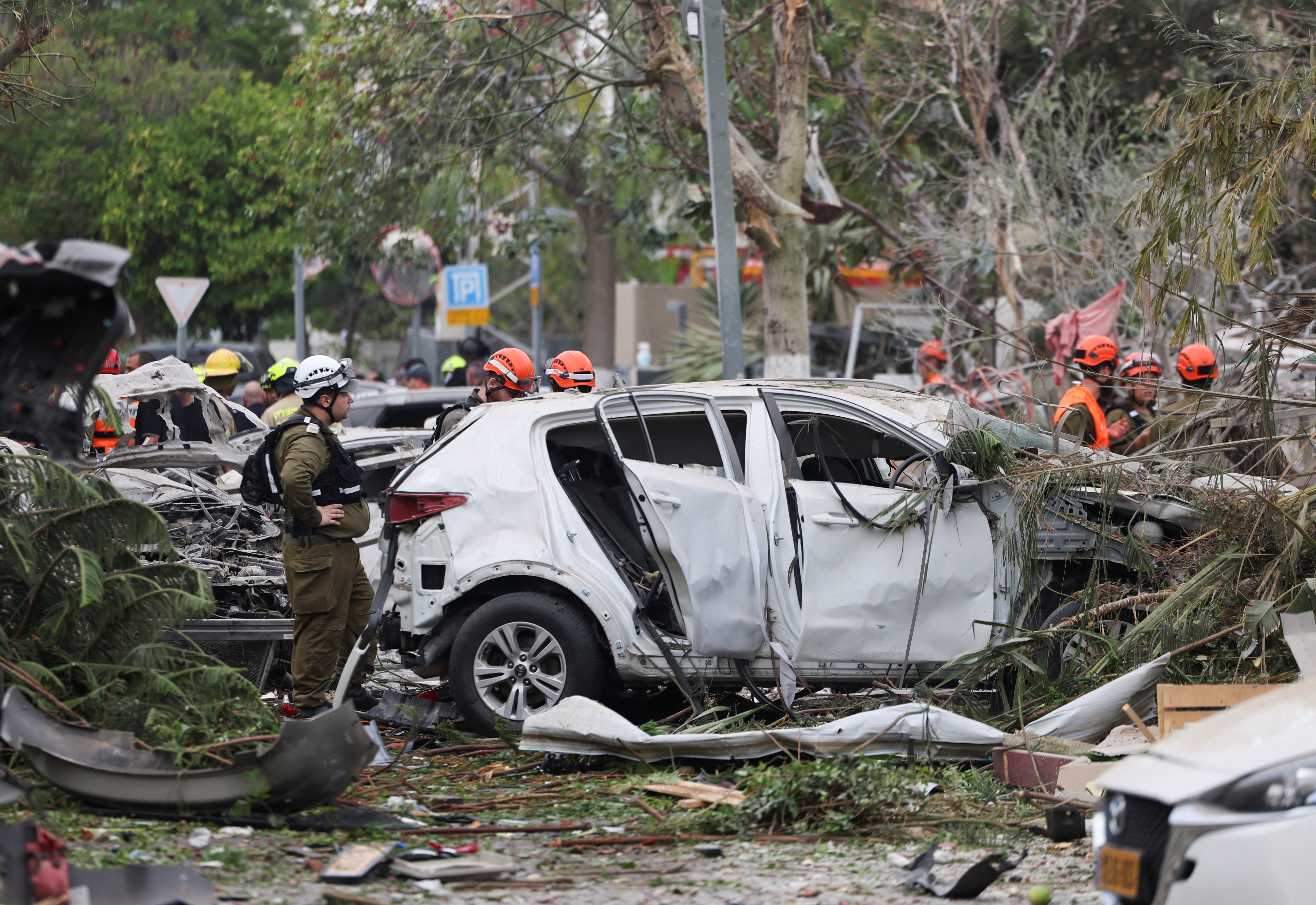 Rescue personnel stand next to the remains of a car, destroyed in an Iranian attack in Rishon LeZion, Israel.