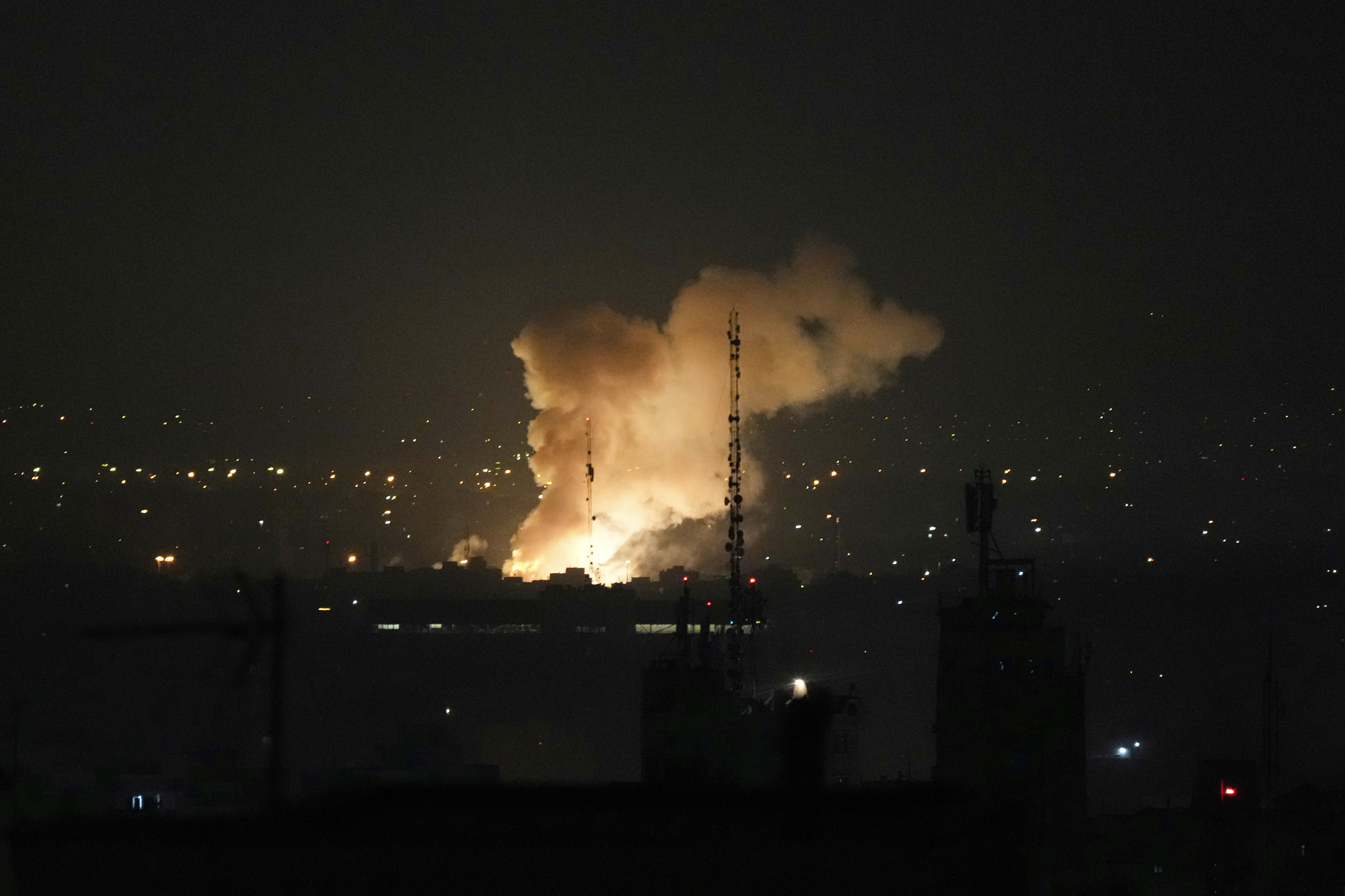 Large fire and smoke rising over a city at night.