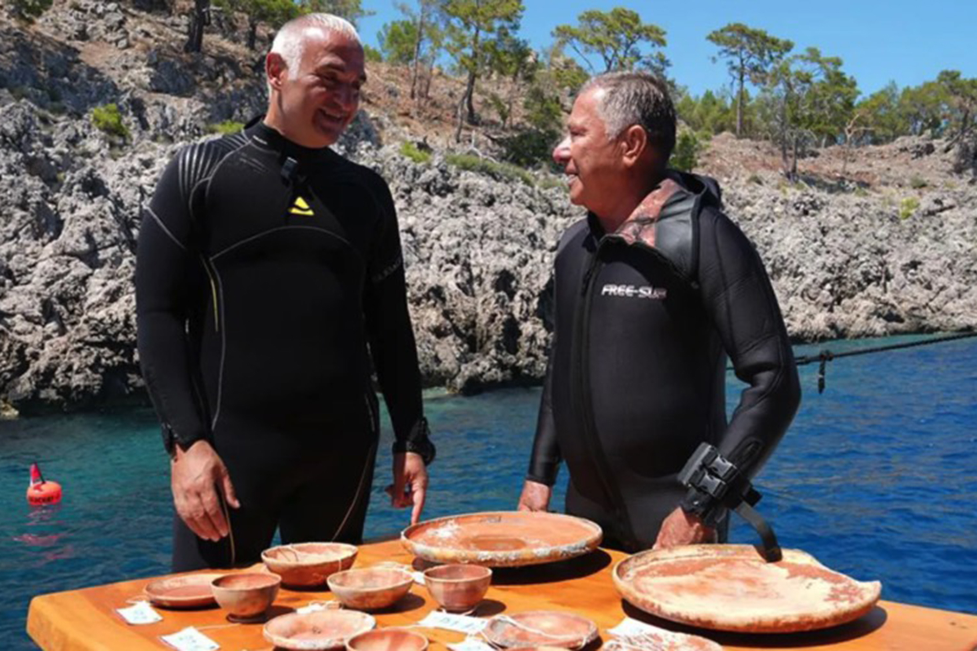 Two men in wetsuits display ancient pottery recovered from a 2,000-year-old shipwreck off the coast of Turkey.