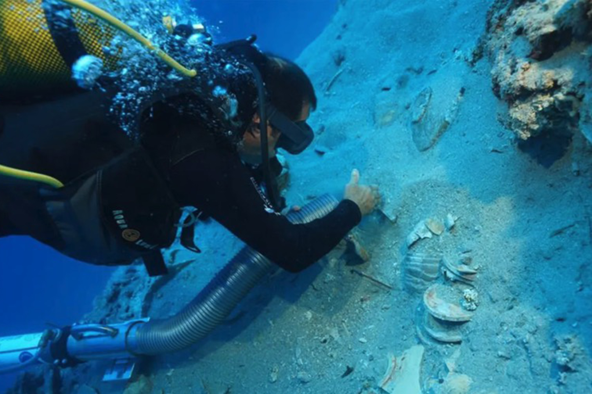Diver examining ancient ceramics at a 2,000-year-old shipwreck.