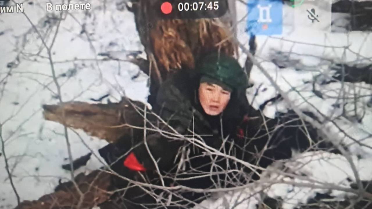North Korean soldier taking cover behind trees in snowy conditions.