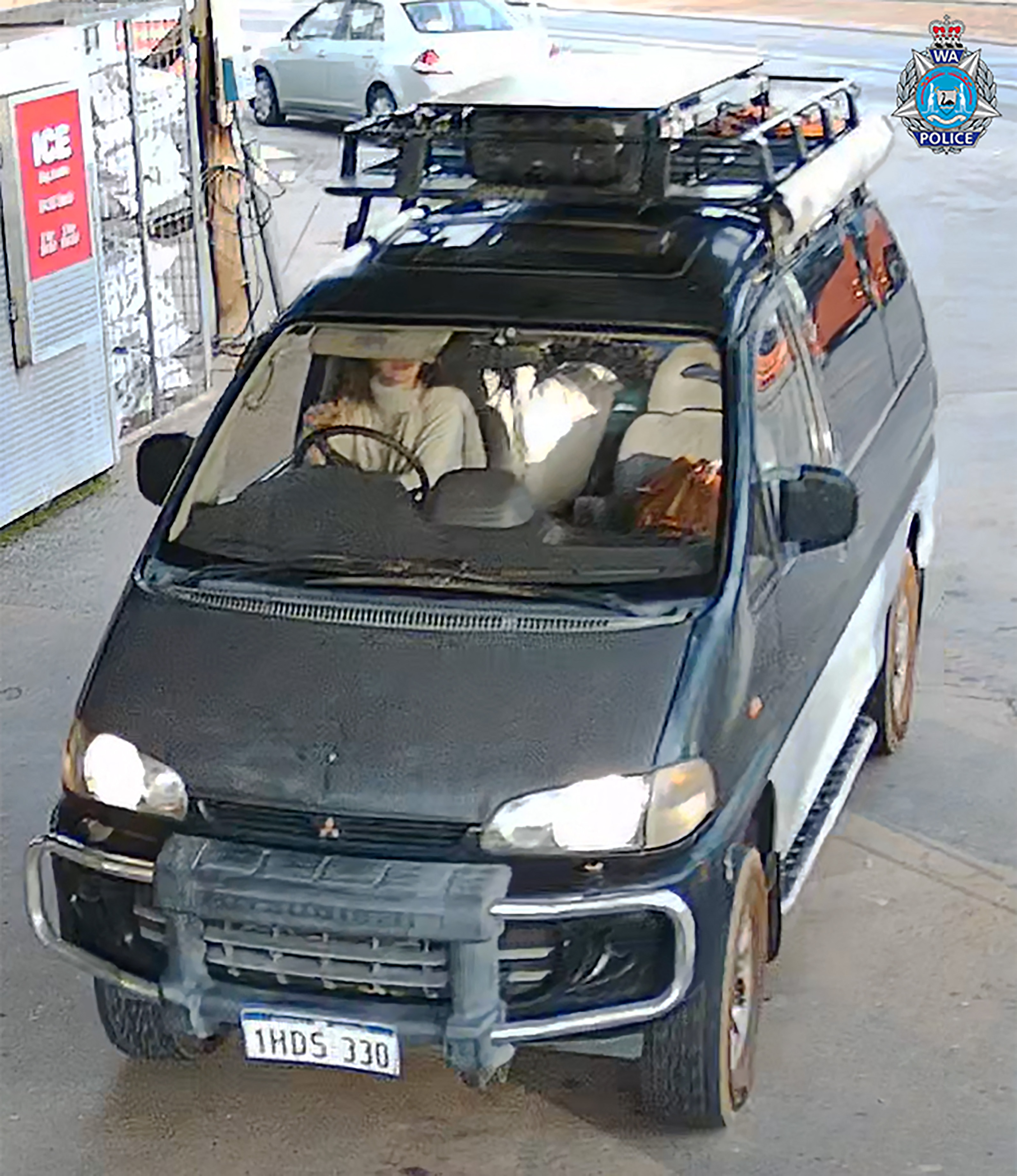 Photo of a dark-colored van with a roof rack, license plate 1HDS 330, and a woman inside.