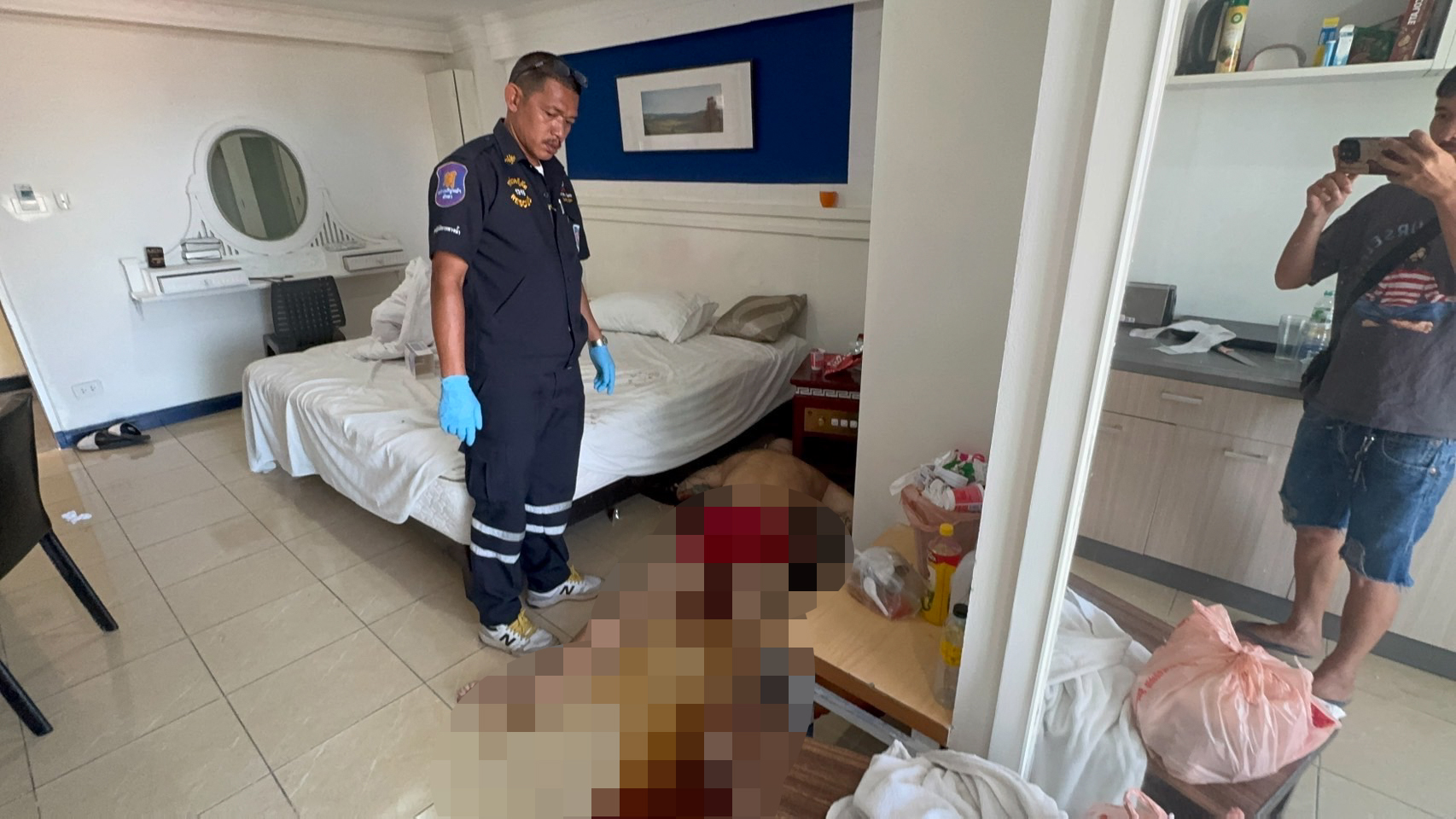 Crime scene photo: a dead man lies on the floor of an apartment, with a first responder present.