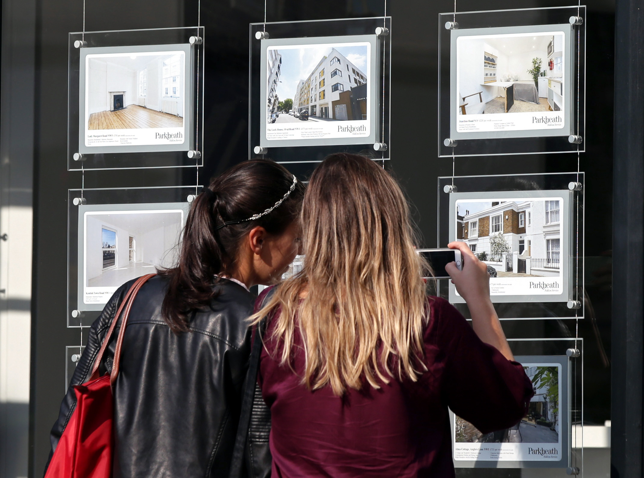 Two women looking at real estate listings in an estate agent's window.