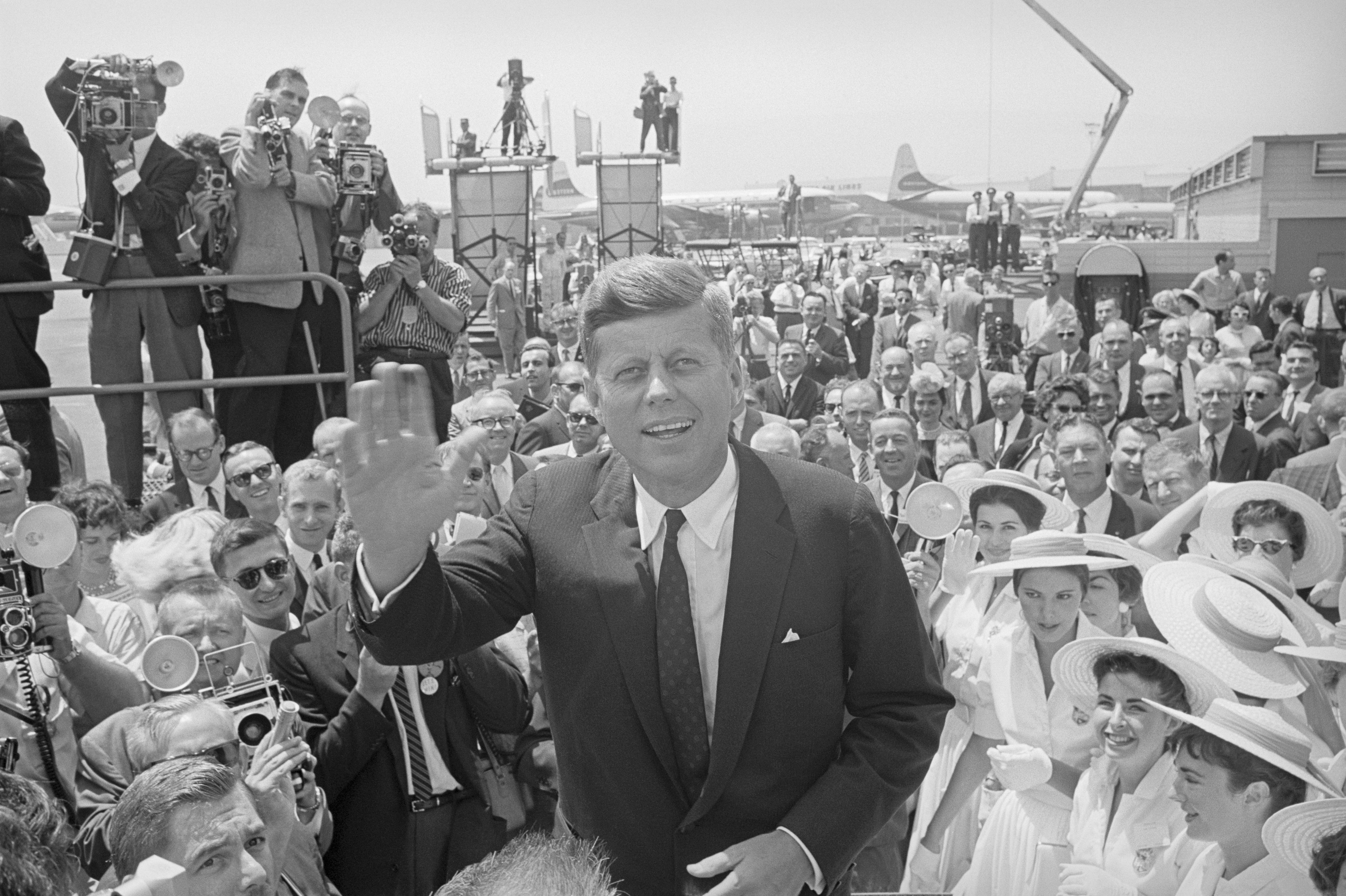 John F. Kennedy waving to a large crowd at an airport.