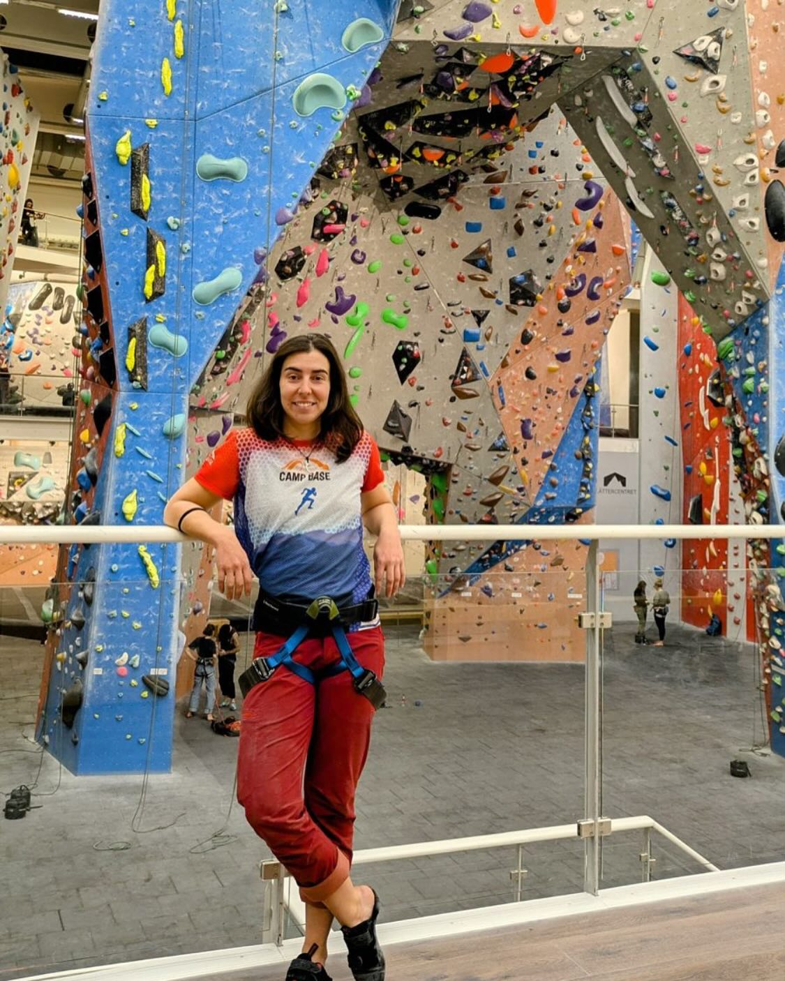 Woman in climbing gear stands in front of an indoor climbing wall.