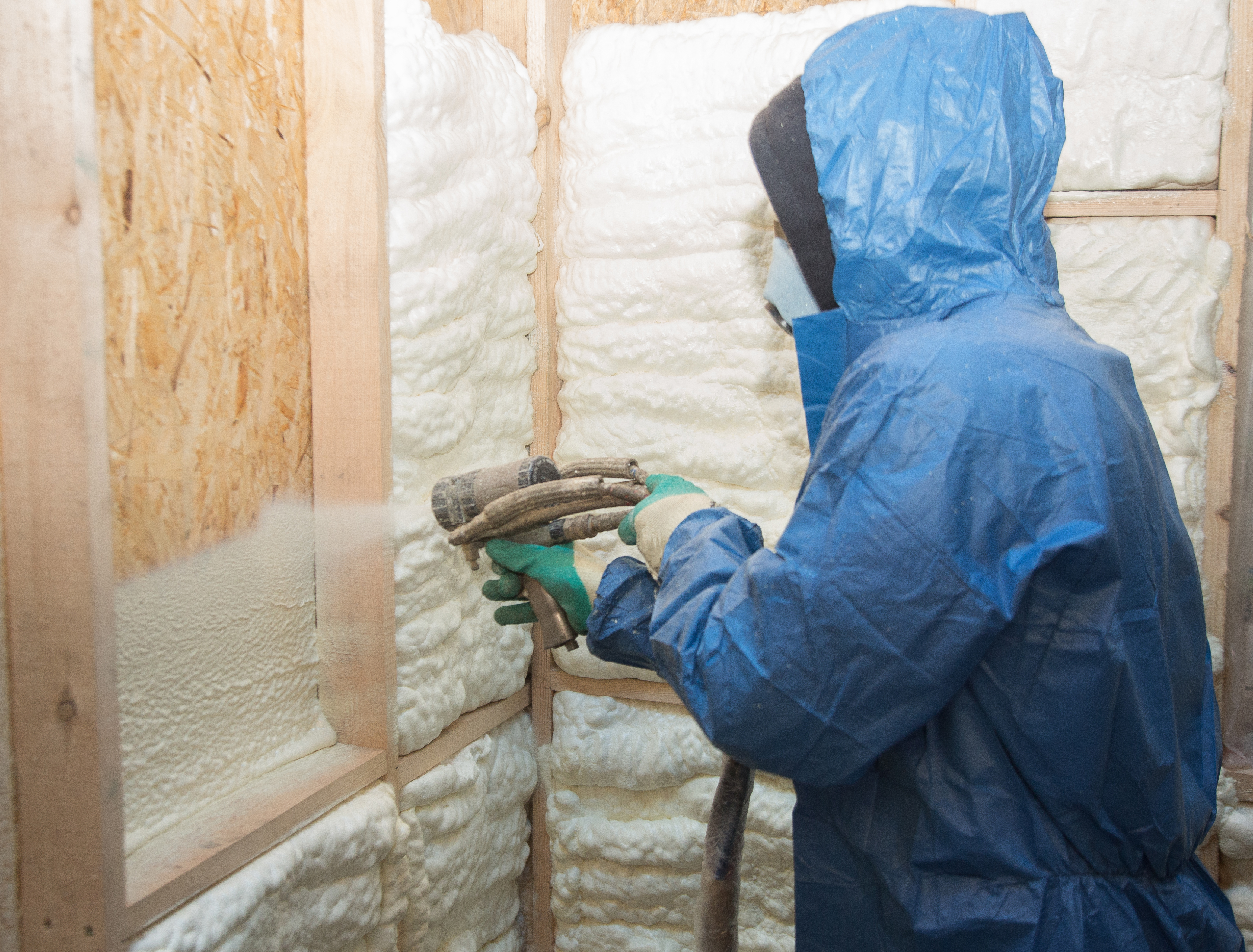 Worker spraying foam insulation into a house wall.